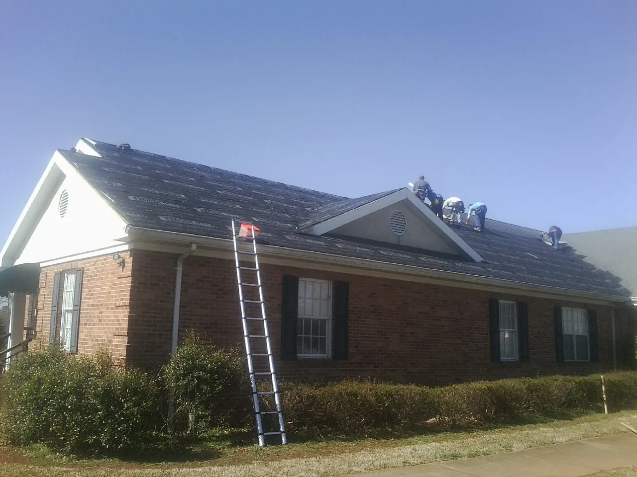 Crew tearing shingles off a brick ranch roof with a ladder set — Emergency Roof Repair work by our crew in Clifton