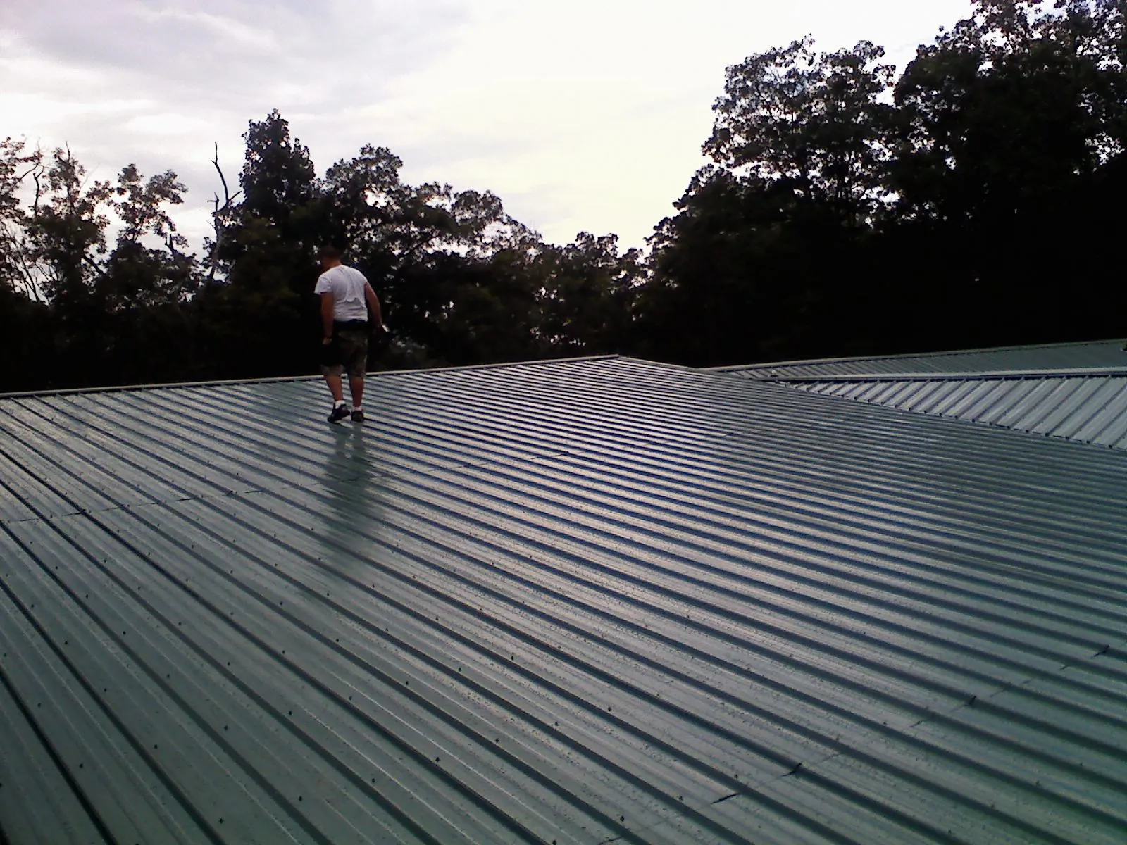 Roofer walking a wide expanse of new green metal roofing in Clifton