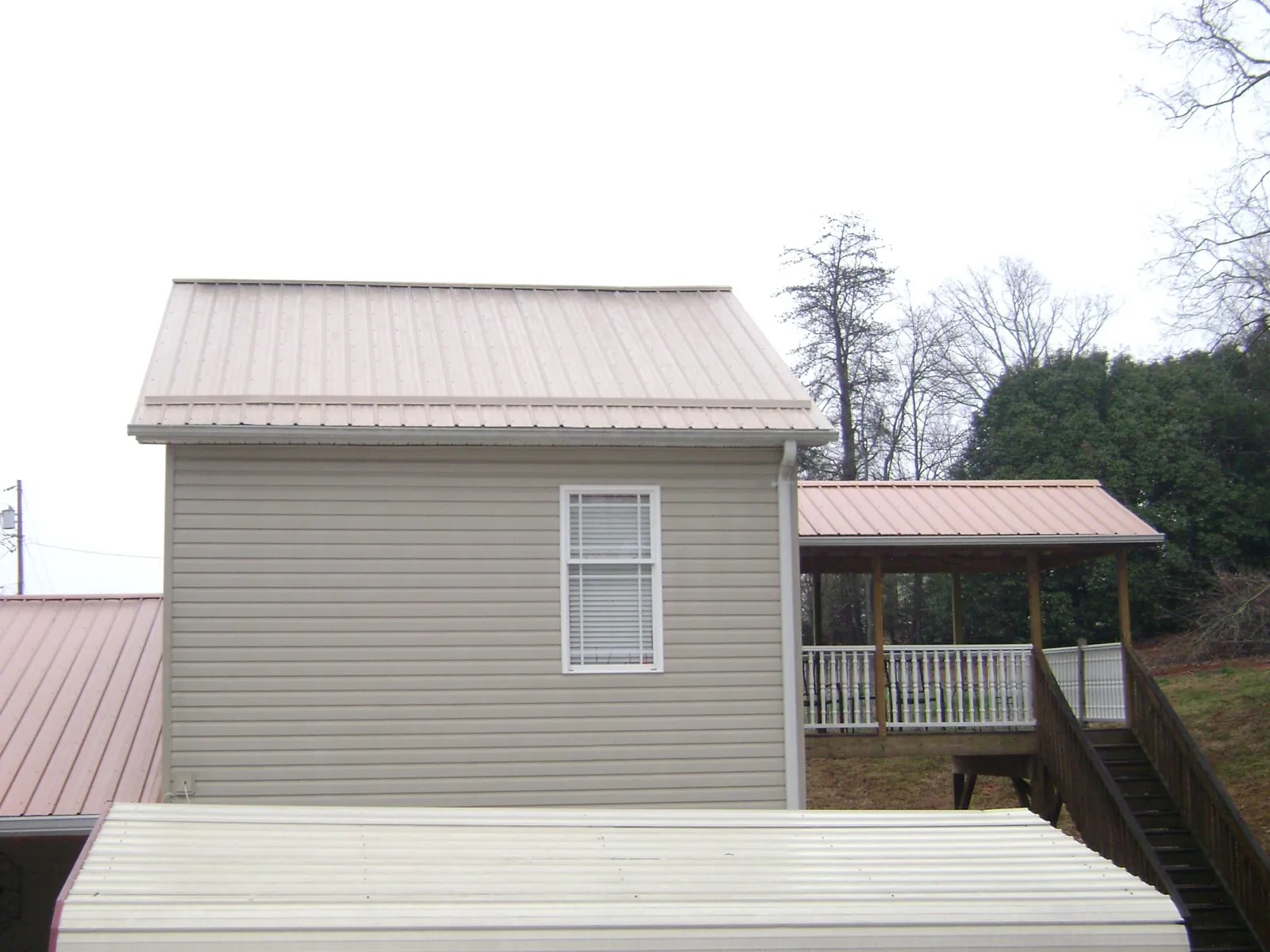 Tan metal roofs on a two story addition and attached porch, from a Roof Replacement job in Clifton